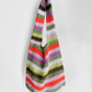 A handmade crochet shoulder bag with horizontal stripes in orange, red, pink, purple, green, brown, and white, hanging against a plain light gray background.