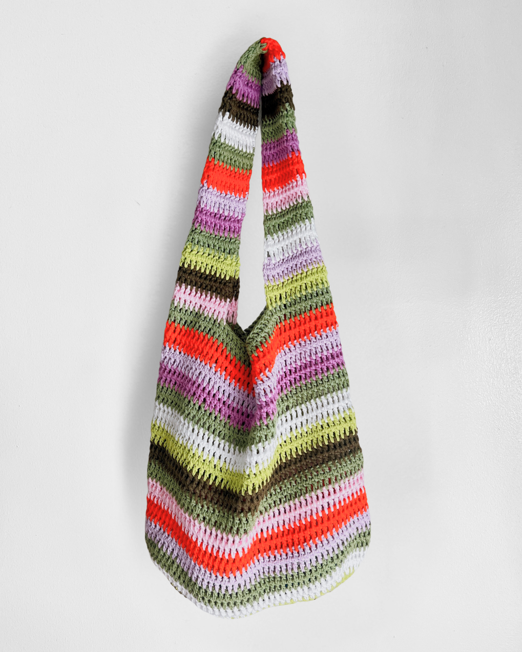 A handmade crochet shoulder bag with horizontal stripes in orange, red, pink, purple, green, brown, and white, hanging against a plain light gray background.